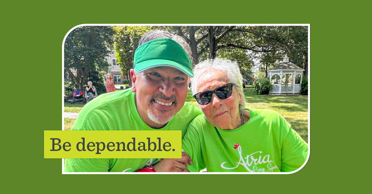 A man wearing a green visor hugs an older woman. Both people are wearing bright green Atria Bay Spring shirts. A lime green overlay says, 